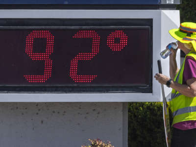 A crossing guard stands next to a sign that says 92 degrees