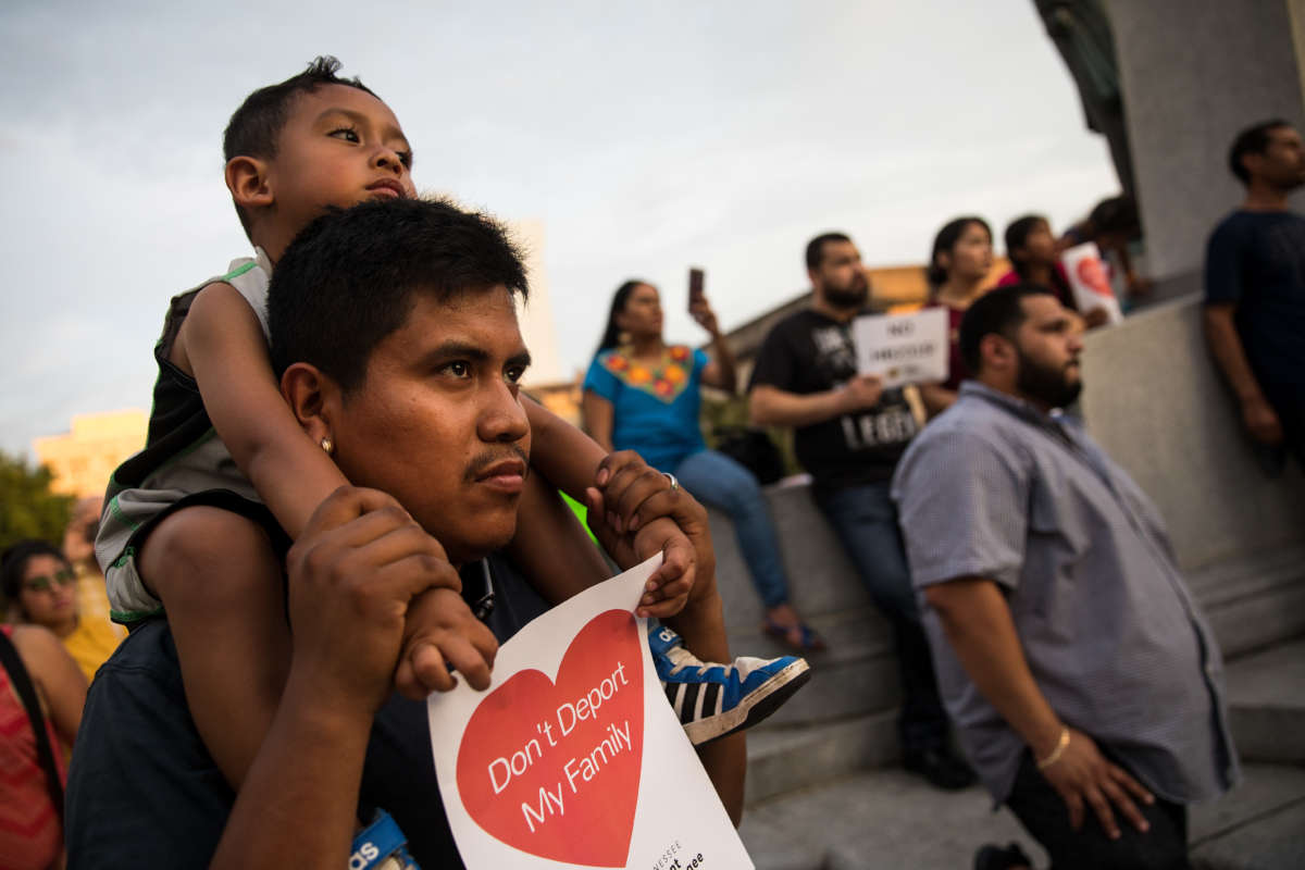 Young child on his father's shoulders holding a sign that says "Don't deport my family"