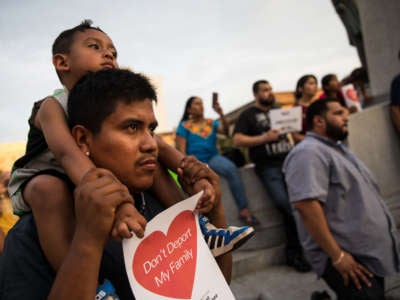 Young child on his father's shoulders holding a sign that says "Don't deport my family"