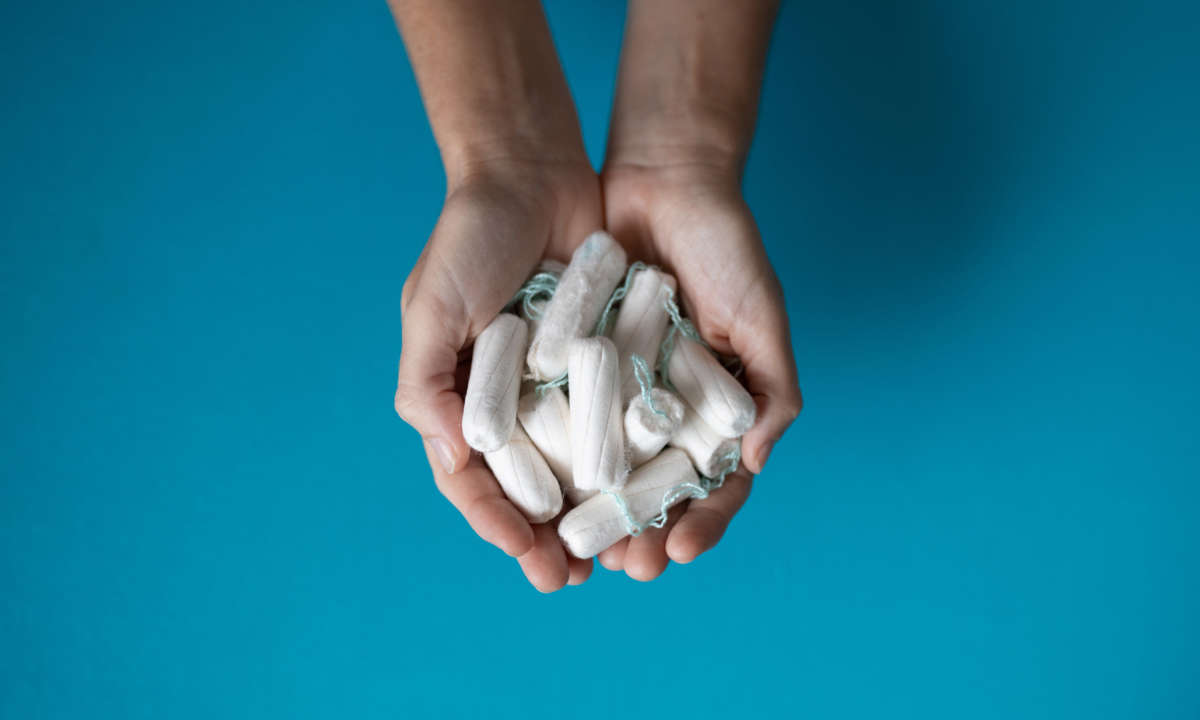 Hands hold several tampons in front of blue background