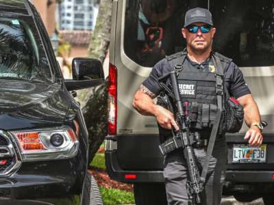 A member of the secret service walks toward the camera, holding a gun