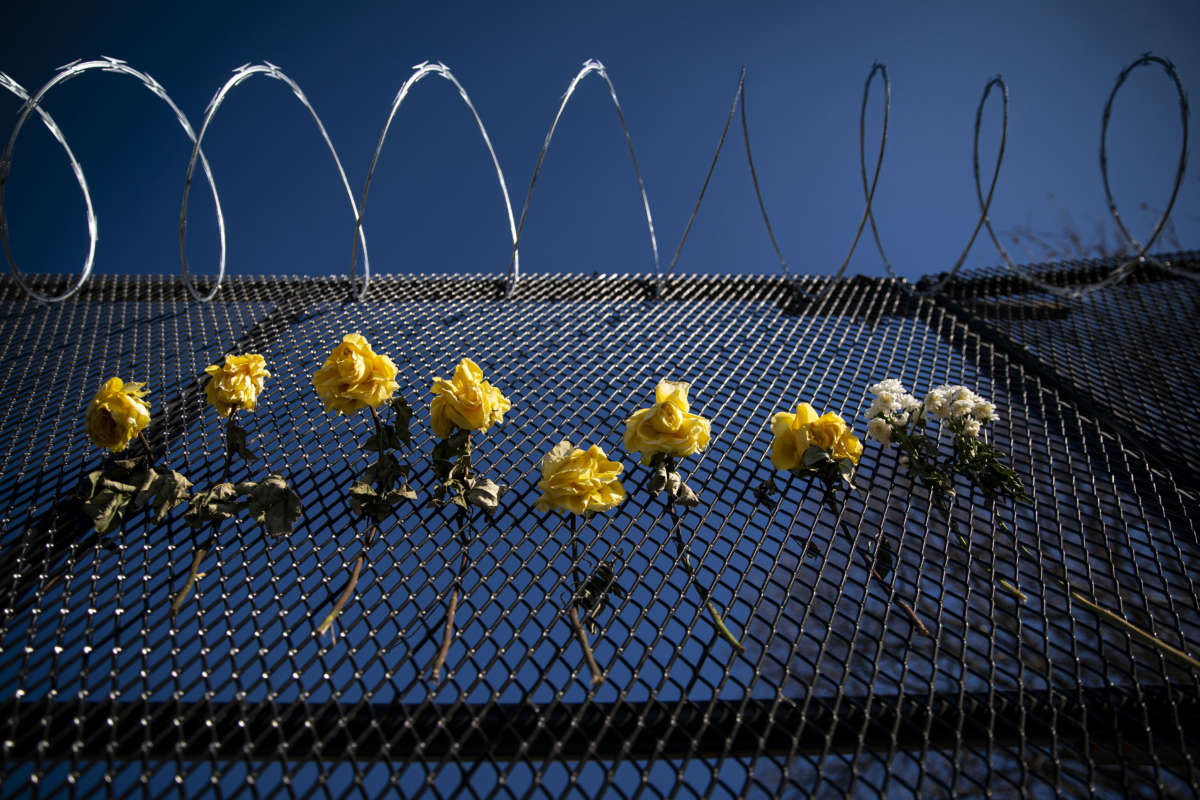 Flowers hang on a barbed wire security fence.