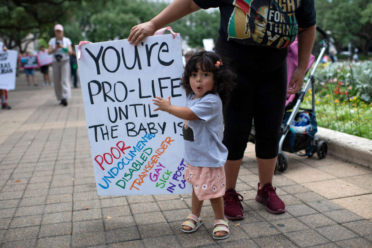 A toddler points to a sign held by her parent that reads 'you're pro-life until the baby is poor / undocumented / disabled / transgender / gay / sick / in foster care" at an abortion rally in Texas