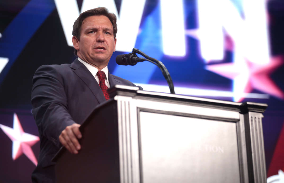 Florida Gov. Ron DeSantis speaks at a rally from behind podium with the word 'win' visible behind him