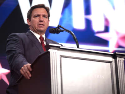 Florida Gov. Ron DeSantis speaks at a rally from behind podium with the word 'win' visible behind him