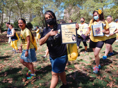 Masked marchers in matching yellow shirts carry photos of their loved ones that had passed away due to complications from covid