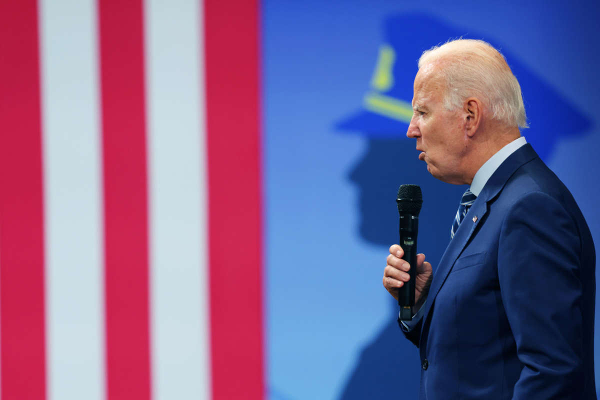 Joe Biden speaks into a microphone in front of an illustration of a cop