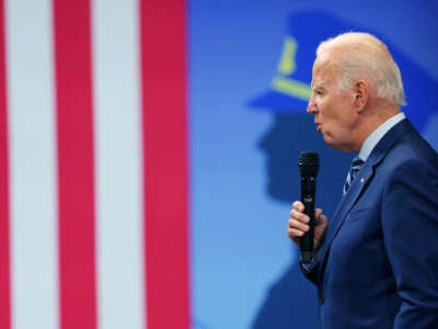 Joe Biden speaks into a microphone in front of an illustration of a cop