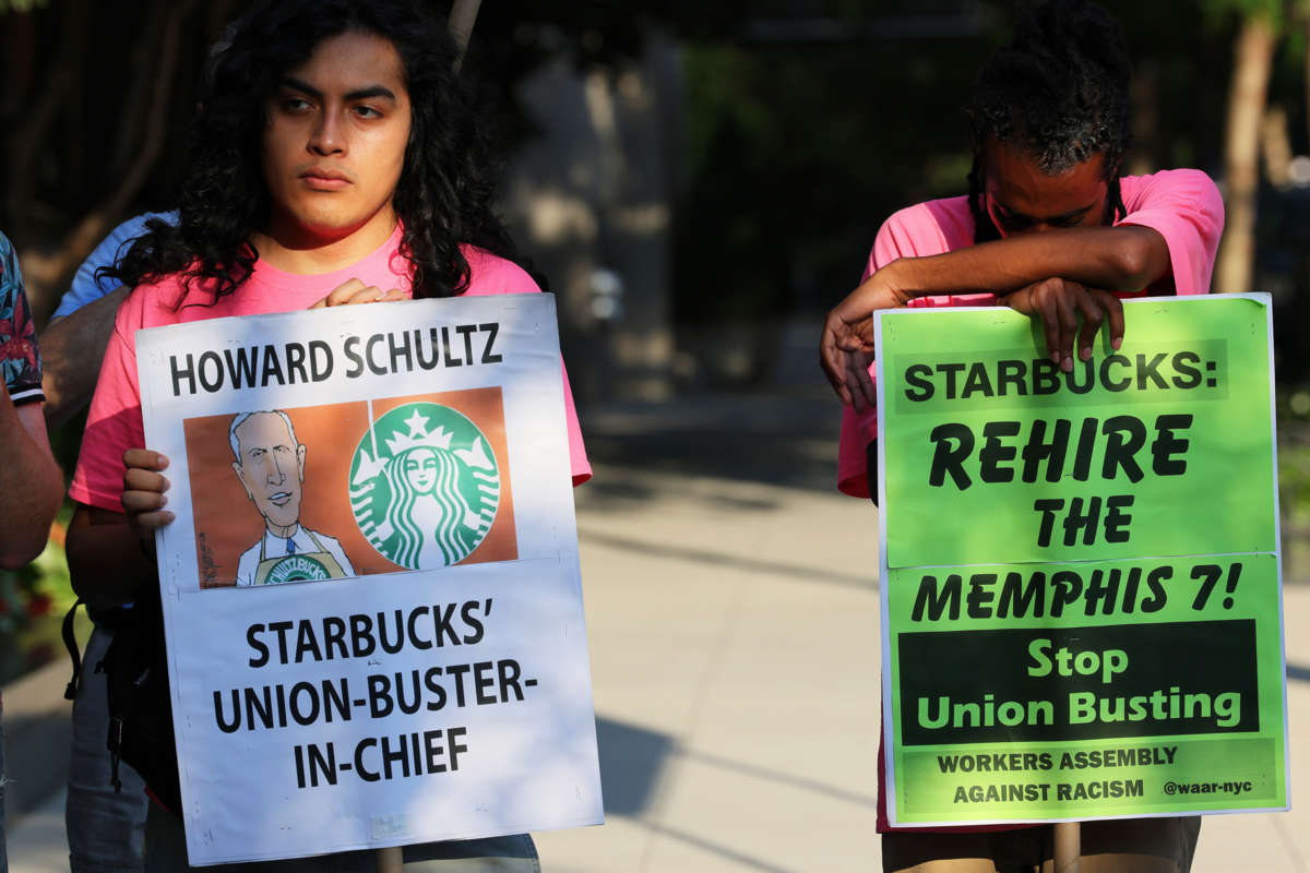 A protester holds a sign reading "HOWARD SHULTZ: STARBUCKS' UNION-BUSTER-IN-CHIEF" during an outdoor demonstration