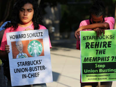 A protester holds a sign reading "HOWARD SHULTZ: STARBUCKS' UNION-BUSTER-IN-CHIEF" during an outdoor demonstration