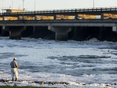 A person fishes in a river foaming with pollution