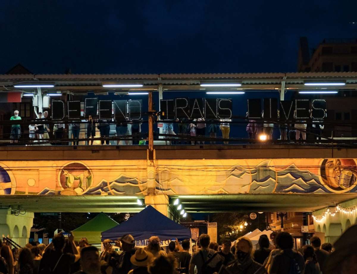 A group of activists hold lighted letters spelling out the words 'SAVE TRANS LIVES' on the Morse elevated train overpass in Chicago