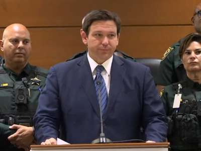 Florida Gov. Ron DeSantis stands at a podium with law enforcement officers lined up behind him