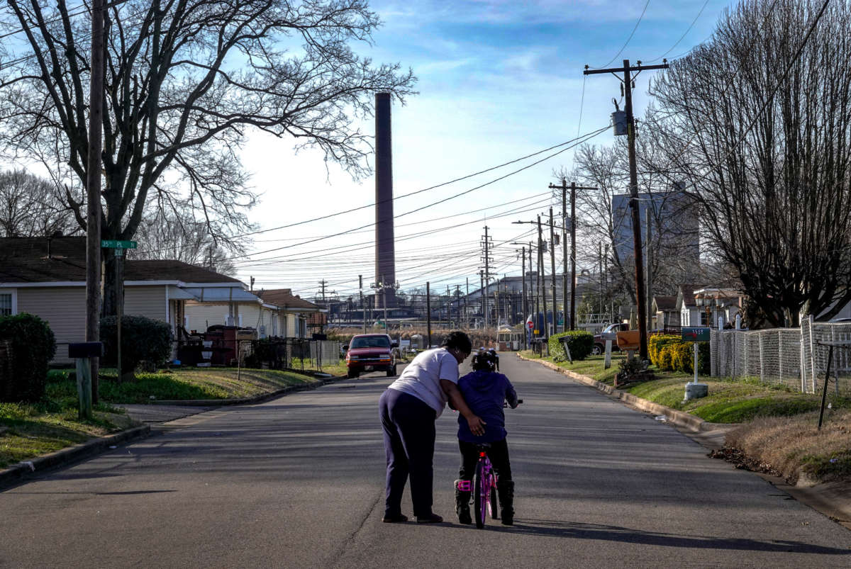A parent teaches her child to ride without training wheels as a smoke stack from ERP Coke juts above the landscape in Birmingham, Alabama, on January 7, 2018.
