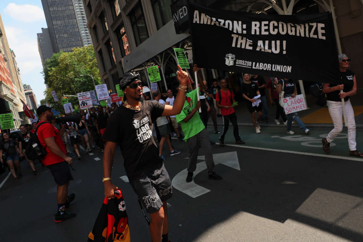 Christian Smalls, President of the ALU, leads pro-union protestors on a march down a New York street. Many carry signs, one prominent banner reads 'Amazon: Recognize the ALU!'