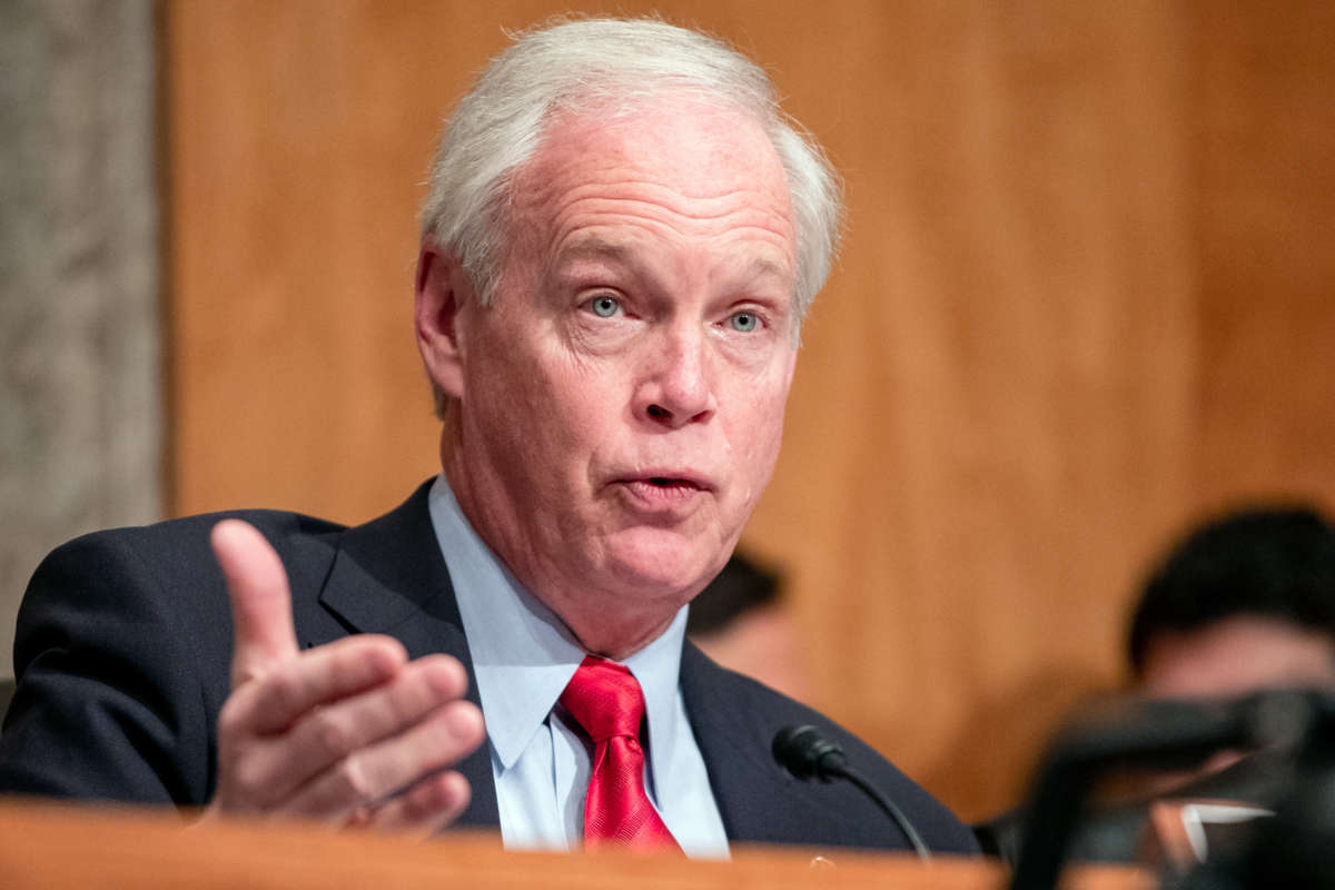 Sen. Ron Johnson, right hand raised outward, speaks into a microphone at a hearing at the U.S. Capitol