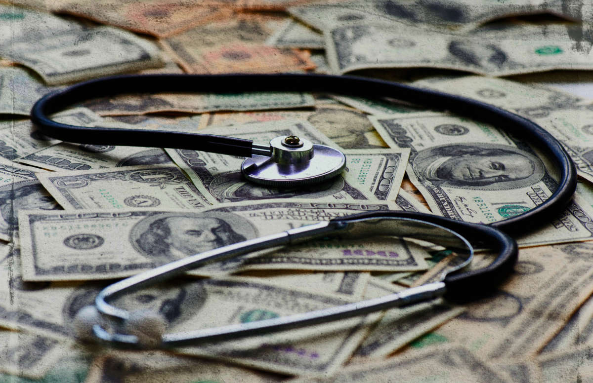 Stethoscope lying on top of hundred dollar bills, image distressed