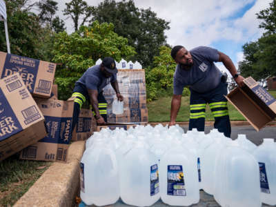 Two men unbox gallon jugs of water