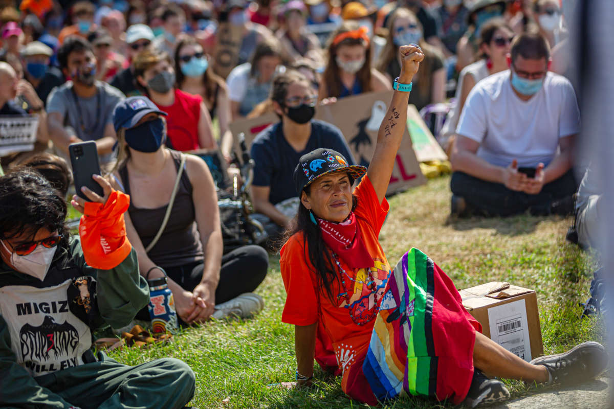 A woman raises a fist while sitting with other seated protesters at an outdoor event