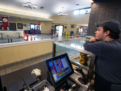 A worker with closed eyes rests atop a display case behind the service counter of a rest stop food court