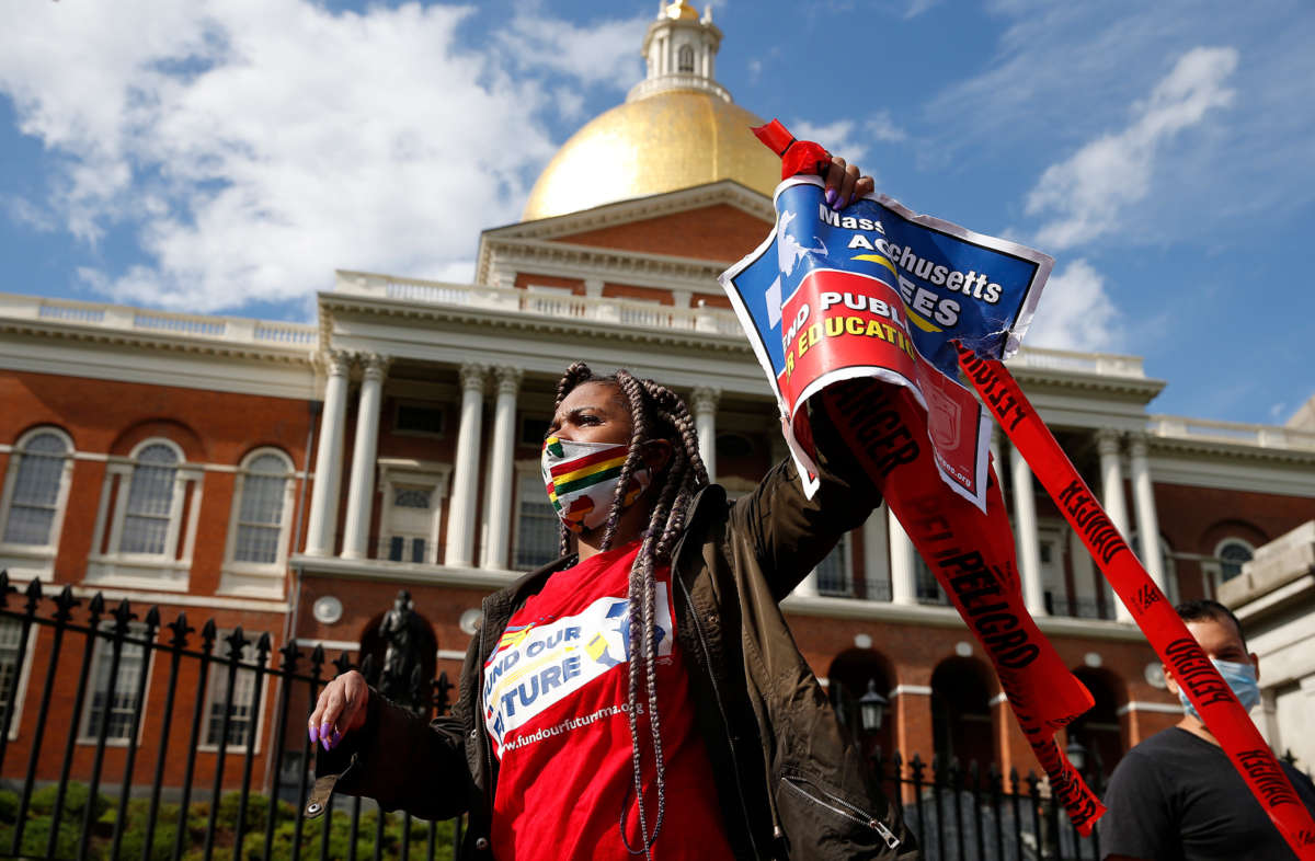 An activist in a mask and a shirt reading "FUND OUR FUTURES" walks