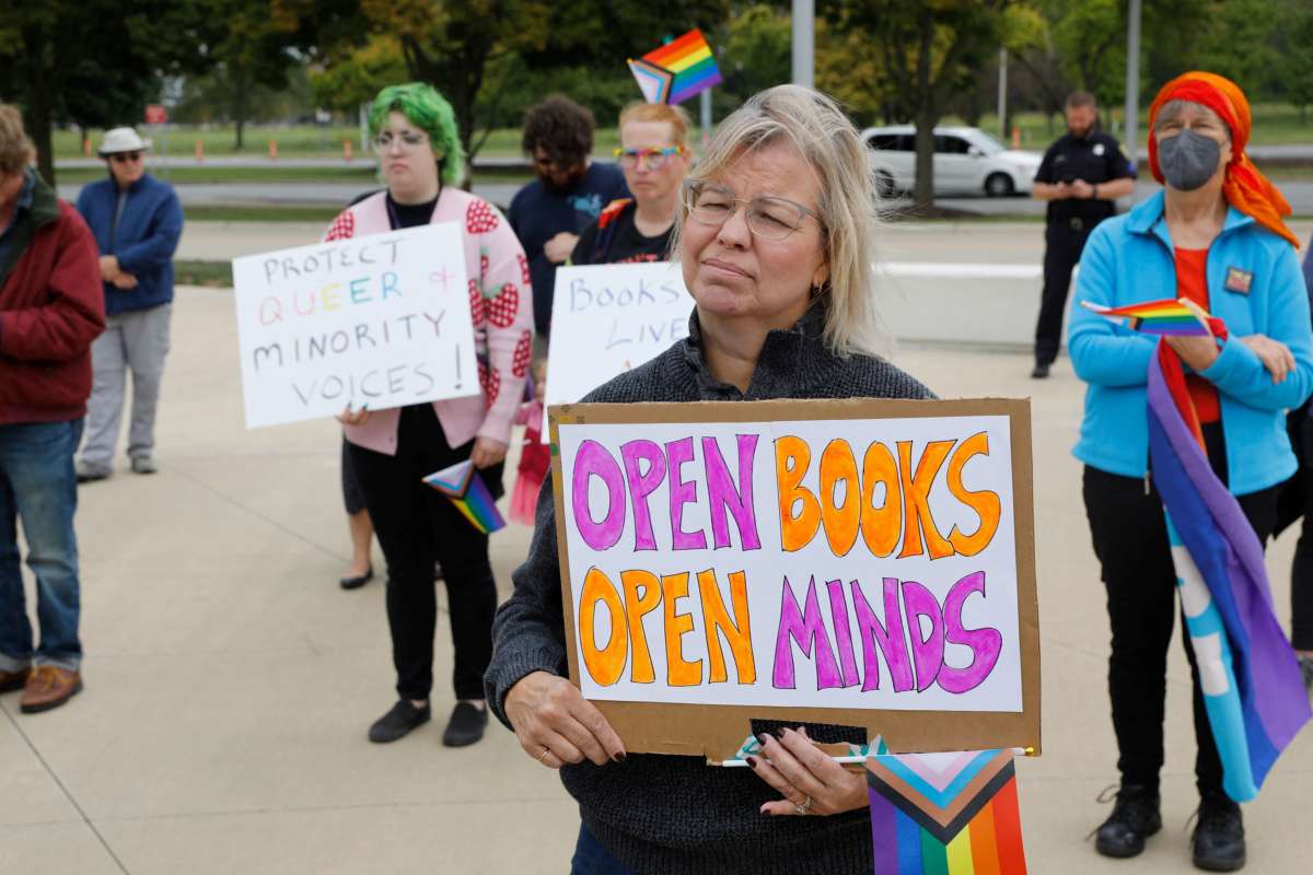 A protester holds a sign reading "OPEN BOOKS, OPEN MINDS" during an outdoor protest