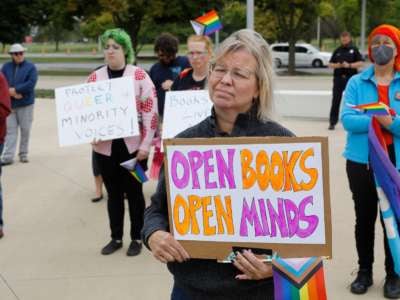 A protester holds a sign reading "OPEN BOOKS, OPEN MINDS" during an outdoor protest
