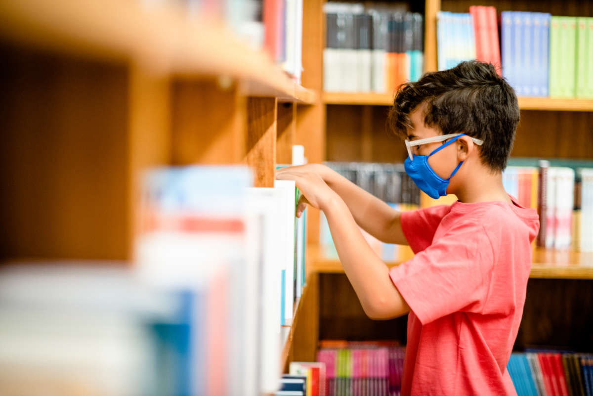 Young boy wearing a face mask browsing shelves at a library