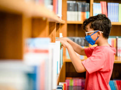 Young boy wearing a face mask browsing shelves at a library