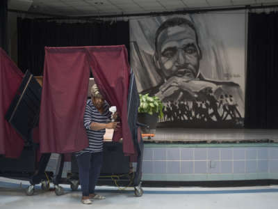 A Black woman leaves a voting booth next to a mural of Martin Luther King Jr.