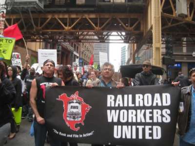 Railroad Workers United march with banner under a bridge