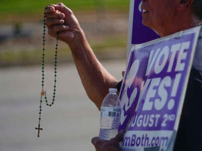 A person is holding up a rosarie while holding a sign in support of a measure voted on earlier this year in Kansas that would have removed abortion protections from the state constitution.