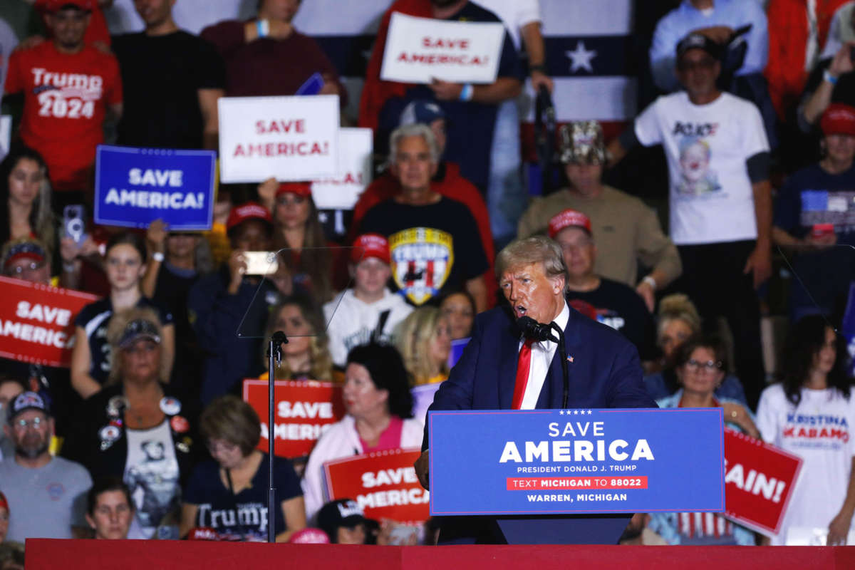 Donald Trump screams into a microphone at a podium in front of his seated supporters