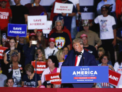 Donald Trump screams into a microphone at a podium in front of his seated supporters