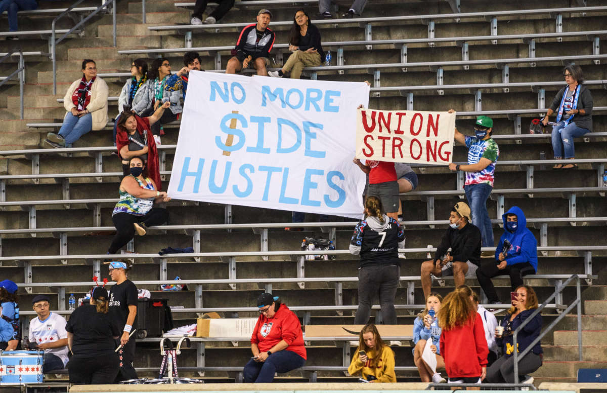 People hold signs saying No More Side Hustles and Union Strong before a game at SeatGeek Stadium on September 25, 2021, in Bridgeview, Illinois.