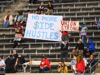 People hold signs saying No More Side Hustles and Union Strong before a game at SeatGeek Stadium on September 25, 2021, in Bridgeview, Illinois.