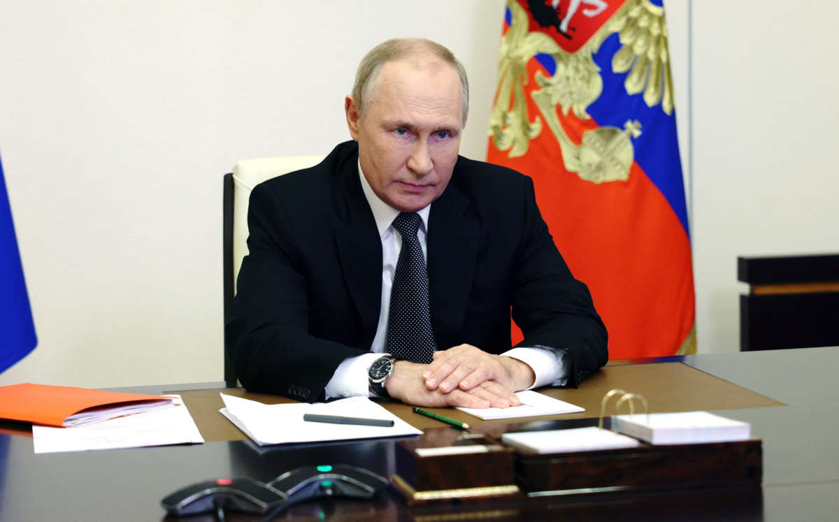 Vladimir Putin sits at a desk and glowers