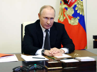 Vladimir Putin sits at a desk and glowers