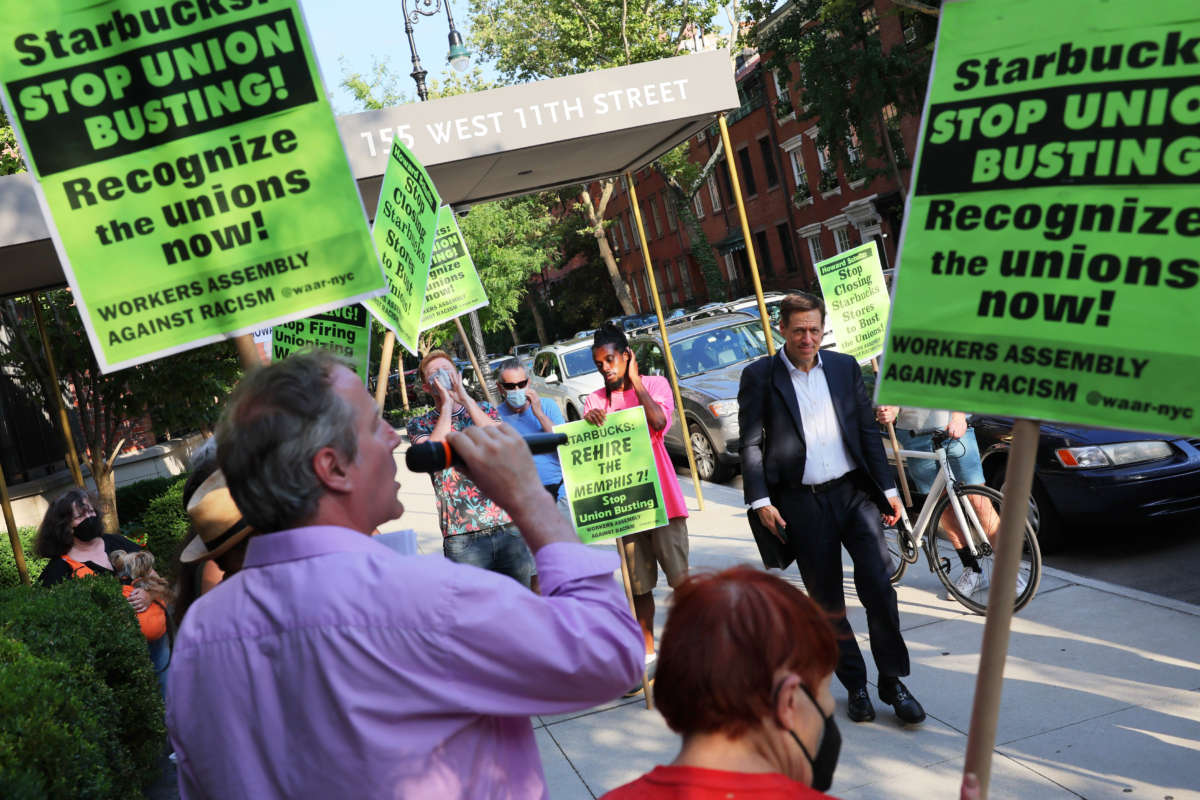 People walk past activists as they participate in a picket line outside Starbucks CEO Howard Schultz on July 19, 2022, in New York City.