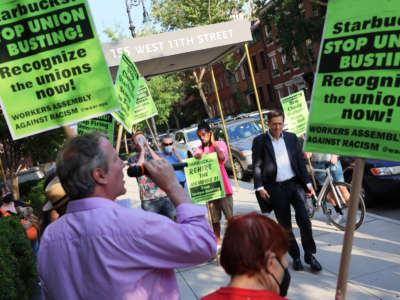 People walk past activists as they participate in a picket line outside Starbucks CEO Howard Schultz on July 19, 2022, in New York City.