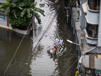 A man walks his bicycle through an intersection flooded with knee-high water