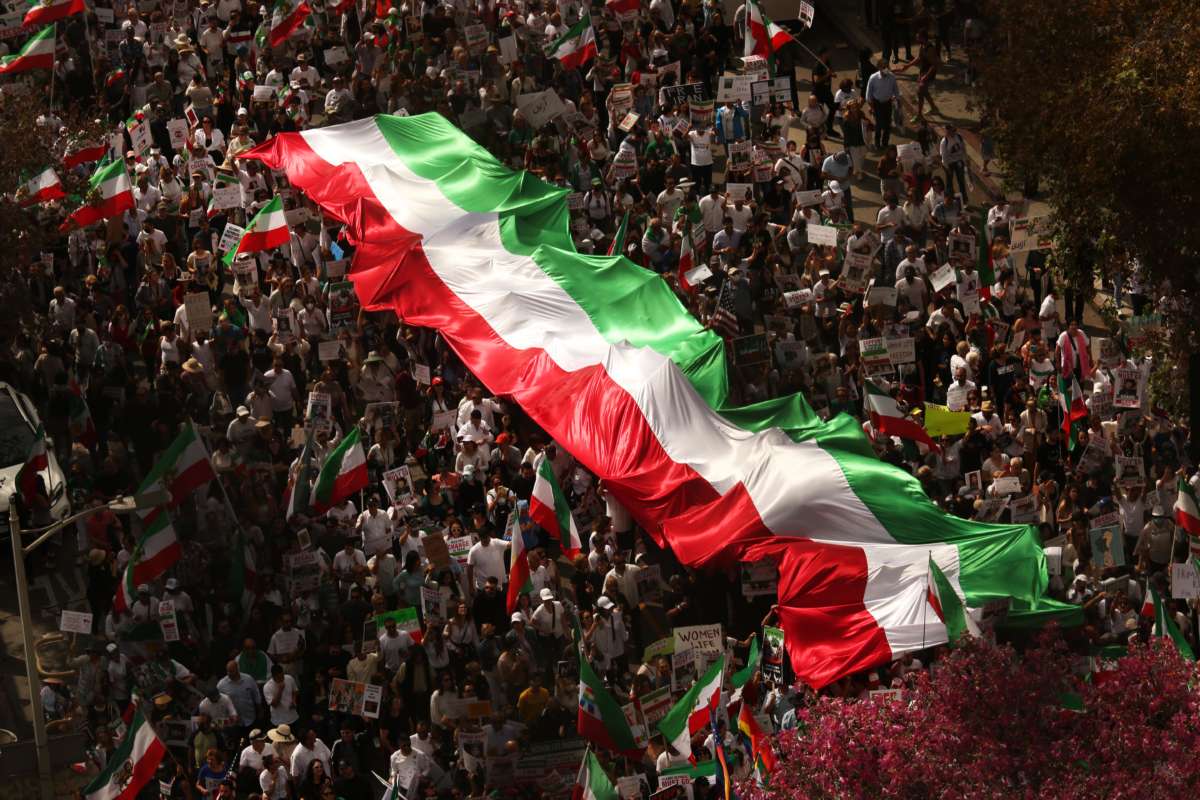 An aerial view of a massive protest wherein people march with a large banner of the Iranian flag