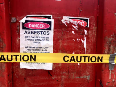 A red dumpster bears a sign warning against exposure to the asbestos held within it
