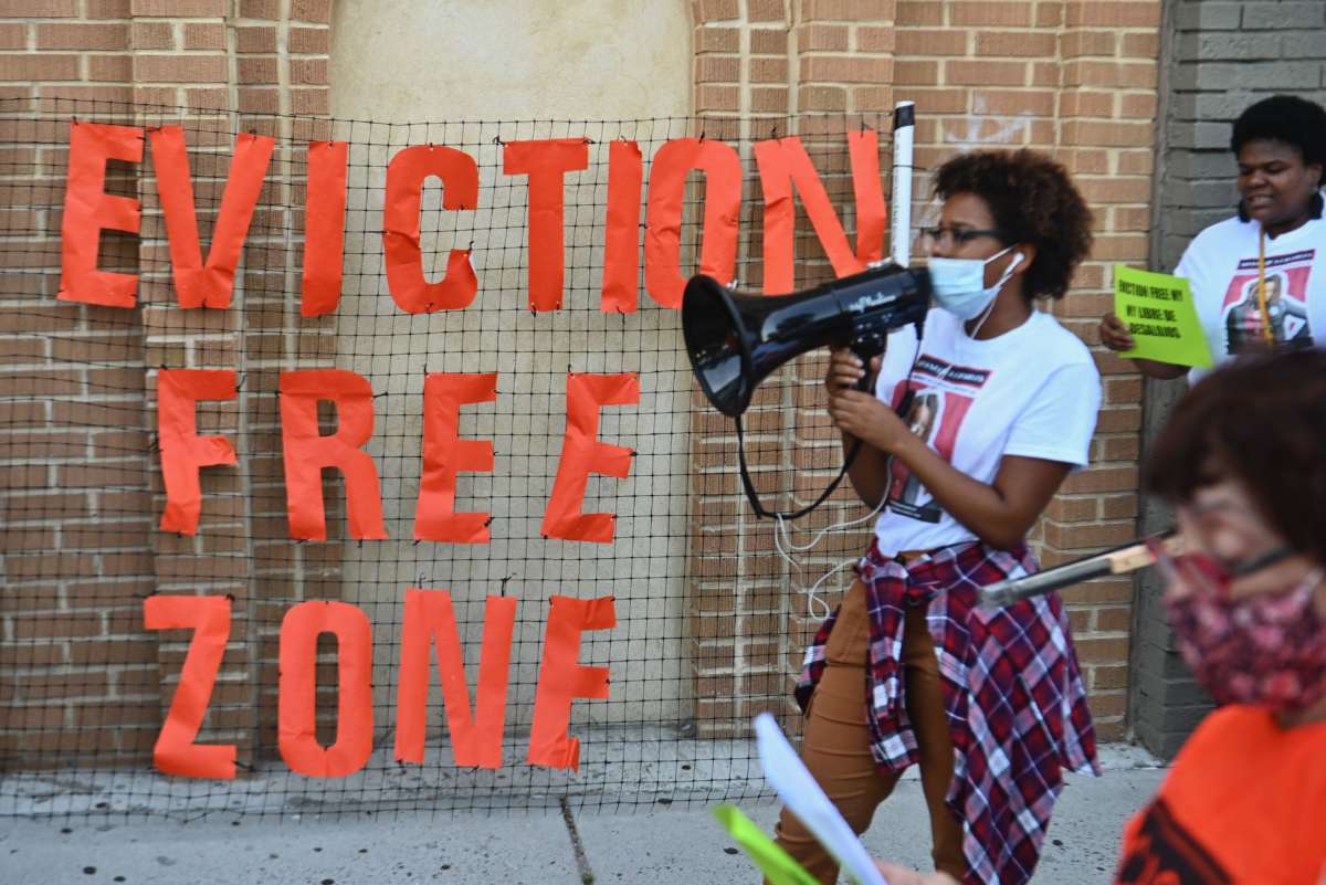 An activist holding a megaphone stands beside a sign saying "eviction free zone"