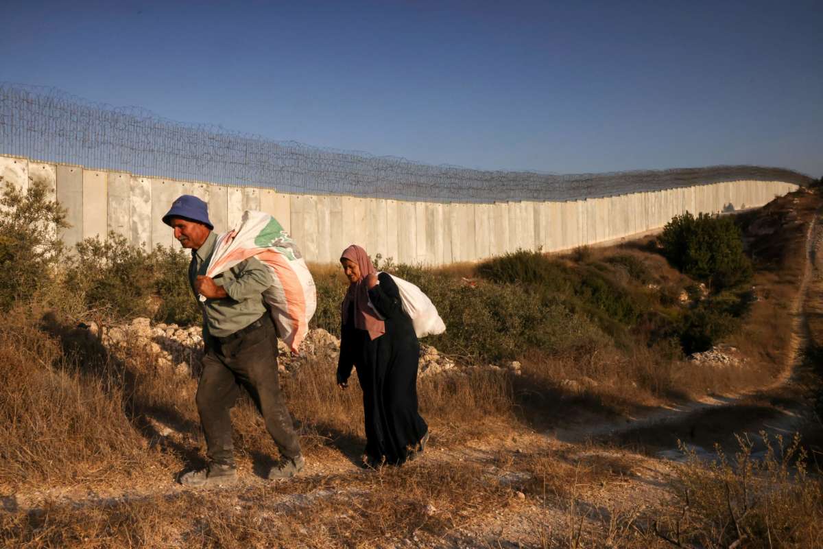 Palestinian farmers walk towards an Israeli checkpoint before attempting to cross into their land, which was divided by Israel's separation wall, near the West Bank village of Bayt Awwa, on October 22, 2022.