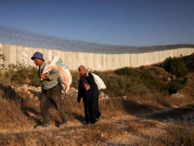 Palestinian farmers walk towards an Israeli checkpoint before attempting to cross into their land, which was divided by Israel's separation wall, near the West Bank village of Bayt Awwa, on October 22, 2022.
