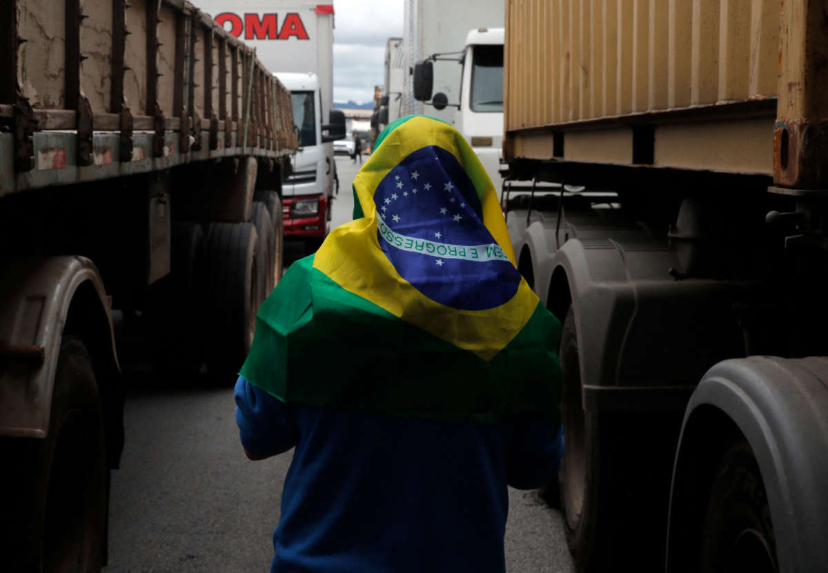 A supporter of recently ousted President Jair Bolsonaro with a Brazilian flag over his head walks between trucks during a blockade on Rodovia Castelo Branco, on the outskirts of São Paulo, Brazil, on November 1, 2022.