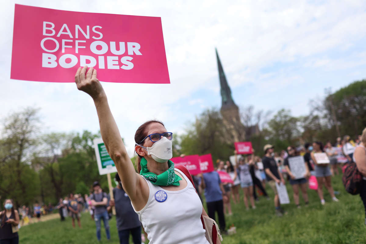 A masked person holds a sign reading "BANS OFF OUR BODIES" during a protest