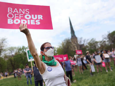 A masked person holds a sign reading "BANS OFF OUR BODIES" during a protest