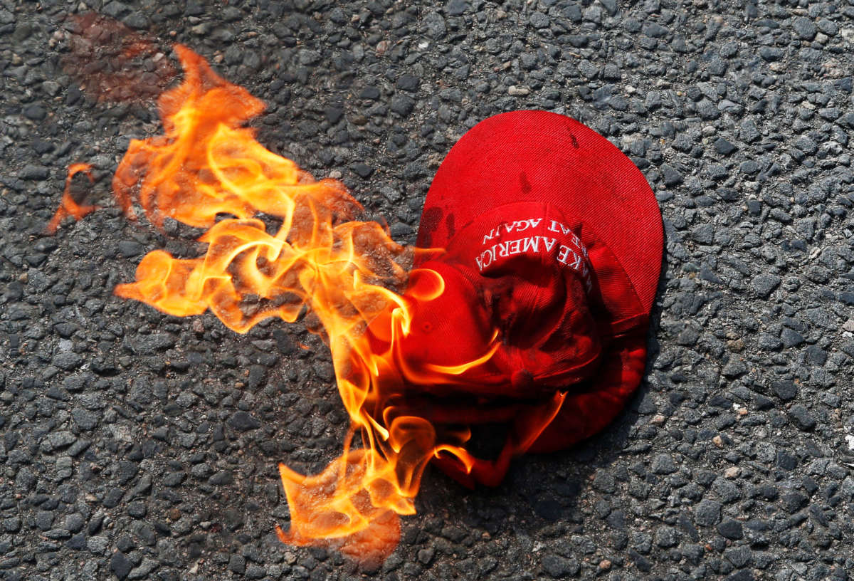 A Make America Great Again hat engulfed in flames burns on the ground at Copley Square in Boston on October 18, 2020.